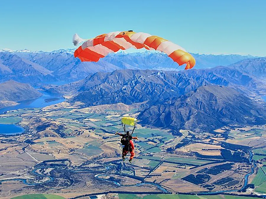 An orange and white parachute above lakes, farmland and mountains